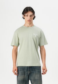 Lys grøn bomulds t-shirt med rund halsudskæring, korte ærmer og hvid trykt tekst "Palm Coast" på venstre bryst.