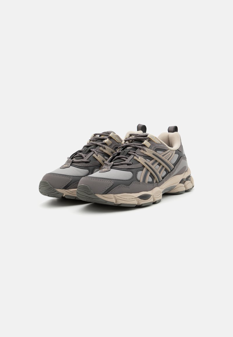 Graue Sportschuhe aus einer Kombination von glatten und strukturierten Materialien, mit einer beigen Sohle und einem detaillierten Schnürsystem. Akzente in hellgrau.