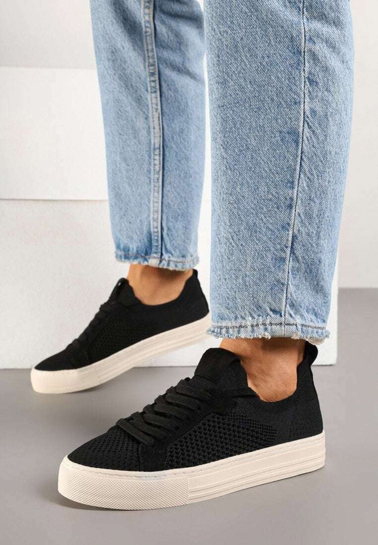 Baskets noires avec un dessus en maille texturée et une semelle en caoutchouc blanche, associées à un jean court bleu clair avec un ourlet effiloché.