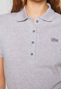Polo gris en tissu texturé. Il comporte un col, une patte de boutonnage à trois boutons et un petit logo brodé sur le côté gauche.
