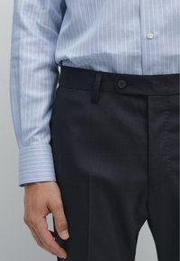 Lichtblauw, verticaal gestreept overhemd met knopen bij de kraag; donker op maat gemaakt broek met een enkele knoop en zijzakken.