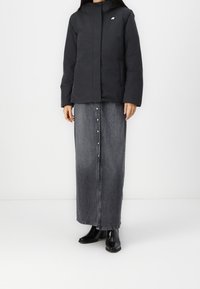 Černá prošívaná bunda se zipem vpředu a kapucí. Kombinována s tmavě modrou džínovou maxi sukni s centrálním knoflíkovým zapínáním a černými kotníkovými botami.