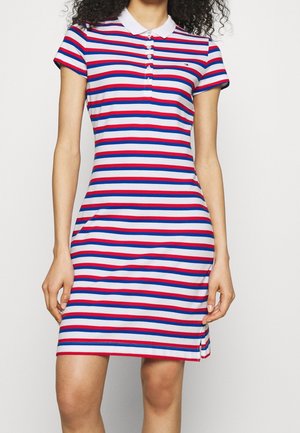 Femme portant une robe polo à manches courtes, longueur genou, avec des rayures horizontales rouges, blanches et bleues et un col blanc.