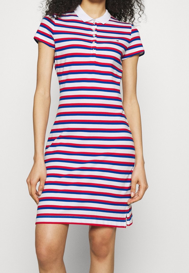 Femme portant une robe polo à manches courtes, longueur genou, avec des rayures horizontales rouges, blanches et bleues et un col blanc.