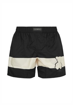 Black and white swim shorts with elastic waistband, horizontal white stripe, and abstract bear design on the right leg. Brand label on waistband.