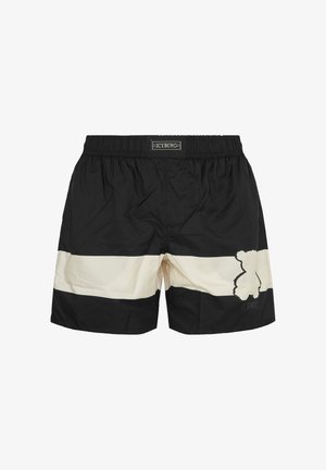 Costume da bagno nero e bianco con elastico in vita, striscia bianca orizzontale e design astratto di orso sulla gamba destra. Etichetta del marchio in vita.