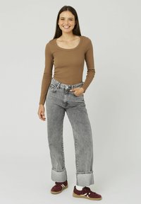 Haut marron à manches longues avec un décolleté arrondi, associé à un jean taille haute gris clair avec des ourlets retroussés. Baskets bordeaux avec des accents blancs.