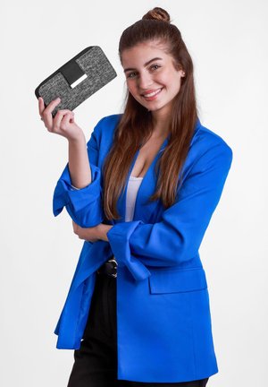 Black and grey wallet with a textured finish and a strap closure, held by a person in a blue blazer. Background is white.