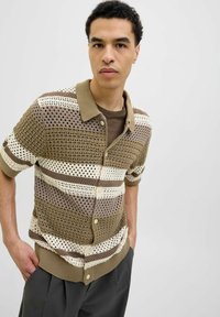 Camicia a pulsanti in maglia con un motivo di fori geometrici, presenta righe marroni, crema e beige, maniche corte e un colletto testurizzato.