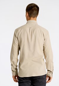 Camisa de hombre de manga larga, color beige claro, con cuello abotonado, pliegue en la parte posterior y puños abotonados, fabricada con una tela suave.
