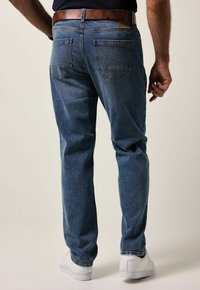 Unos vaqueros de mezclilla en un lavado azul medio presentan un diseño de pierna recta, un desvanecimiento sutil, dos bolsillos traseros y un acento de cinturón de cuero marrón.