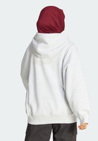 Grå hoodie med dragsko i huvan, ribbade muddar och fåll, bärs med en mörk vinröd hijab. Har en avslappnad passform och mjuk textur.
