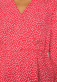 Abito rosso con design avvolgente e scollo a V. Presenta un motivo a cuore bianco, con una texture morbida e un tessuto fluido.