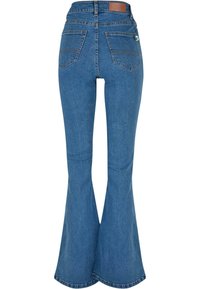 Jeans de mezclilla azul de pata de elefante con cintura alta, que cuentan con dos bolsillos traseros y una etiqueta de cuero en la cintura. Textura suave y acabado limpio.
