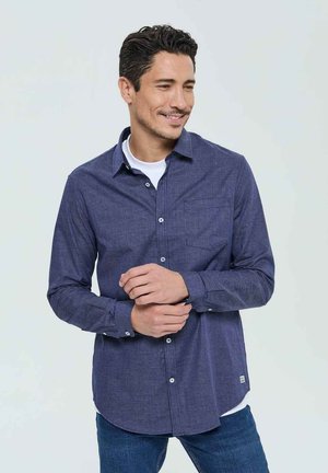 Chemise à carreaux bleu marine avec col boutonné, manches longues et poche avant. Fabriquée en tissu léger avec une texture lisse.