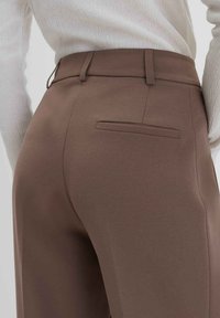 Braune maßgeschneiderte Hosen mit einer glatten Textur, ausgestattet mit einer Gesäßtasche und Gürtelschlaufen. Der Bund ist schlank und strukturiert.