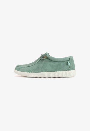 Light green canvas sneaker with a rounded toe, elastic lace, and a white rubber sole featuring a textured pattern. Minimalist design.