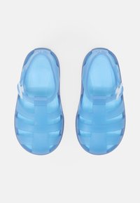 Blue plastic sandals with a strappy design, semi-transparent upper, and solid sole. Features a closed toe and adjustable strap.