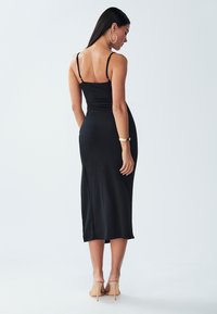 Black, form-fitting midi dress with thin straps, smooth texture, and a subtle sheen. Features a straight hem and back ruching detail.