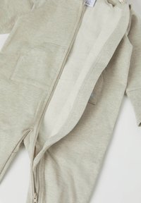 Helles beiges Baby-Overall mit Reißverschluss aus weichem Material, ausgestattet mit einem gefütterten Innenbereich, zwei Fronttaschen und einer Kapuze.