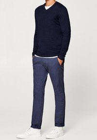 Navy V-neck sweater, knitted fabric; paired with navy trousers, smooth texture, tapered fit; completed with white sneakers.