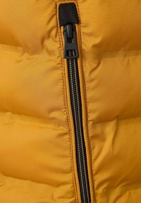 Gelbe Steppweste mit schwarzem Reißverschluss, gestepptem Design und kontrastierendem dunklem Reißverschluss mit metallischen Zähnen.