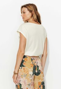 Haut crème à manches courtes avec une coupe ample, associé à un pantalon taille haute à motif floral avec des accents orange et vert.