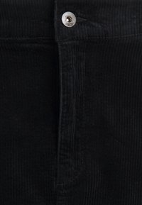 Pantaloni in corduroy neri con righe verticali, dotati di chiusura con bottone metallico e zip frontale. Il tessuto presenta una superficie morbida e texture.