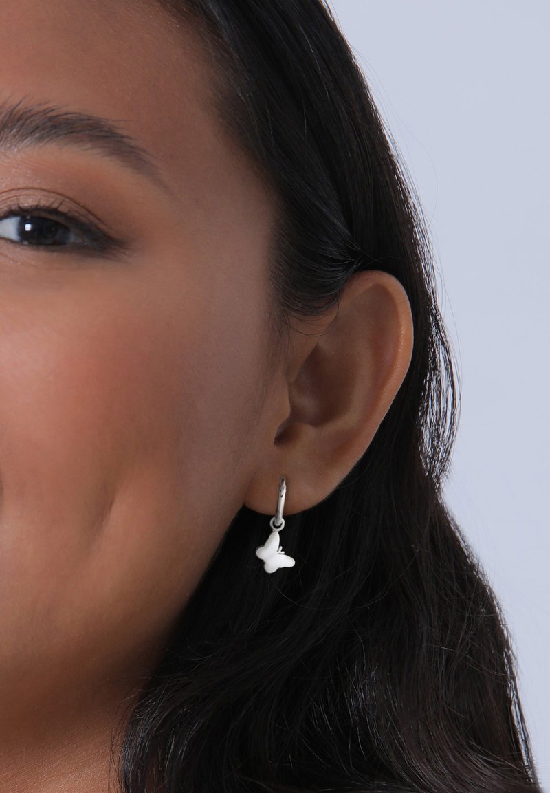 Hvide sommerfugleformede øreringe hængende fra en sølvring, vist på en models øre. Glat, poleret overflade med subtile detaljer.