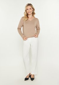 Beige gebreide V-hals trui met lange mouwen, gecombineerd met op maat gemaakte witte broeken en zwarte spitse hakken. Eenvoudig en strak ontwerp.