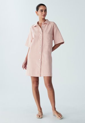 Sukienka z krótkim rękawem i kołnierzykiem w jasnoróżowym kolorze, z przodem zapinanym na guziki, jedną kieszenią na piersi oraz prostym krojem, kończąca się powyżej kolan.