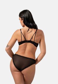 Completo di lingerie con pizzo nero, composto da un bralette con spalline regolabili e mutandine trasparenti abbinate, che mettono in risalto delicati dettagli tessili.