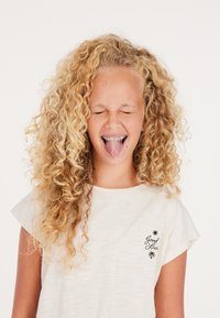 Camiseta corta de manga corta gris claro con cuello redondo, que presenta una impresión negra de un sol y el texto "Buena Suerte" cerca de la parte inferior. Cabello rubio rizado.