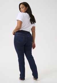 Dark blue denim jeans with a straight-leg fit, featuring two back pockets and visible stitching, paired with a white t-shirt.