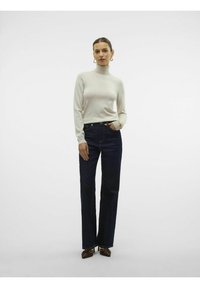 Maglione a collo alto beige chiaro con maniche lunghe, abbinato a jeans a gamba dritta blu scuro a vita alta e scarpe con tacco marroni.