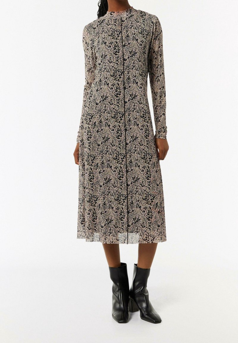 Femme portant une robe midi à manches longues avec un motif abstrait noir et beige et des bottines en cuir noir.