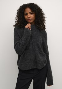 Šedý svetr na zip vyrobený z měkkého, chlupatého materiálu. Disponuje vysokým límcem, velkými předními kapsami a dlouhými, lehce nadměrnými rukávy.