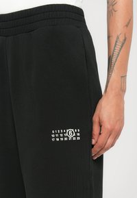 Czarne spodnie dresowe o miękkiej teksturze, z elastycznym pasem i nadrukowaną białą grafiką po prawej stronie, która przypomina kalendarz.