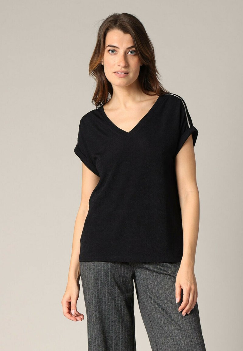T-shirt noir à col en V avec des manches retroussées, fabriqué en tissu doux. Présente un design minimaliste et une fine rayure blanche le long de la couture de l'épaule.