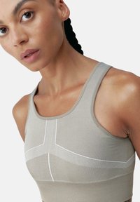 Sportiva di colore beige chiaro con texture a coste, caratterizzata da cuciture bianche decorative e design a corsetto. Vista ravvicinata della scollatura e della zona delle spalle.