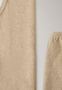 Haut débardeur en tricot beige et pantalon assorti à taille élastique, étalés à plat sur une surface claire, montrant la texture du tissu et les détails des coutures.