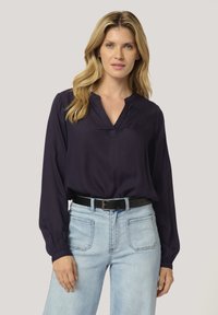 Navy blouse with a V-neckline, long sleeves, and button detail at the collar; paired with light blue jeans and a black belt.