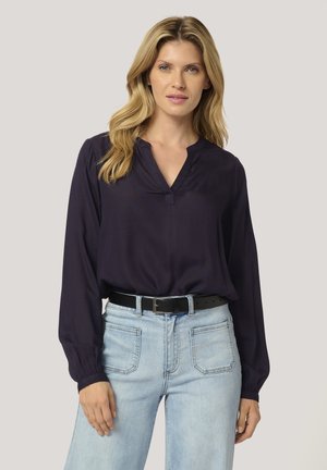 Navy blouse with a V-neckline, long sleeves, and button detail at the collar; paired with light blue jeans and a black belt.