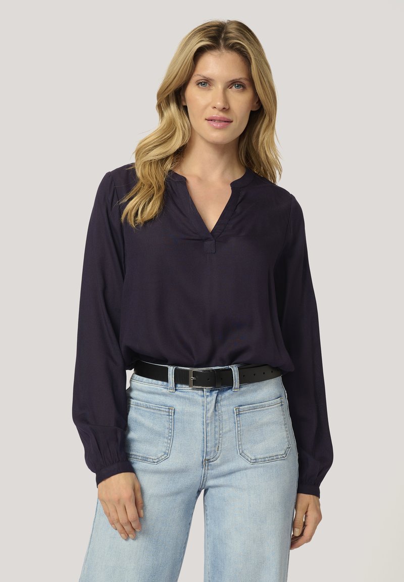 Navy blouse with a V-neckline, long sleeves, and button detail at the collar; paired with light blue jeans and a black belt.