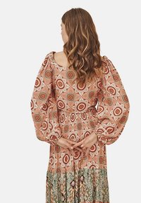 Vestido de manga larga, estilo bohemio, confeccionado con tela ligera. Presenta un estampado floral en colores cálidos, cinturilla fruncida y falda en capas.