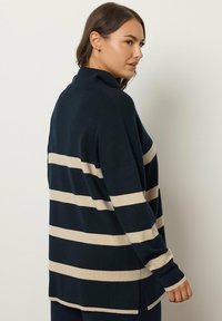 Maglione a maglia blu navy con strisce orizzontali color crema, vestibilità comoda, collo alto, spacchi laterali e maniche lunghe. Texture morbida visibile.