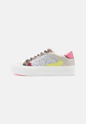 Sneakers feature a beige upper, silver glittery side panel, pink heel accent, yellow detail, and white rubber sole with ribbed texture.