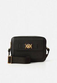 Black leather crossbody bag with a textured surface, gold hardware accents, a front clasp design, and a detachable fabric strap.