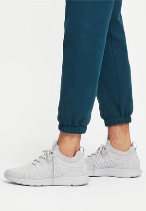 Graue Sportschuhe mit einem Netz-Obermaterial, strukturierten Akzenten und runden Schnürsenkeln, kombiniert mit türkisfarbenen Jogginghosen mit elastischen Bündchen.