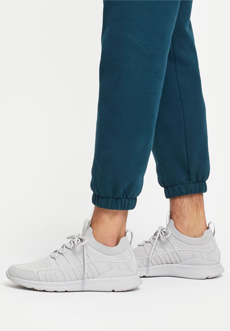 Graue Sportschuhe mit einem Netz-Obermaterial, strukturierten Akzenten und runden Schnürsenkeln, kombiniert mit türkisfarbenen Jogginghosen mit elastischen Bündchen.